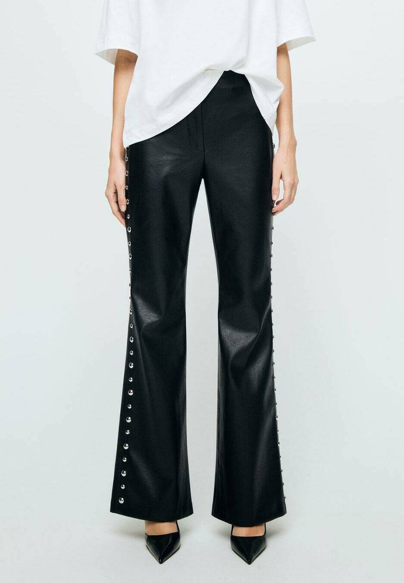 Pantalons évasés en simili cuir noir avec des accents de clous argentés le long des côtés. Texture lisse et design à jambes larges associés à des chaussures pointues noires.