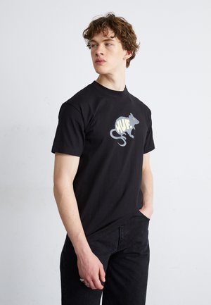 Camiseta de algodón negra con un gráfico de una rata gris y el texto "HUF". Mangas cortas, cuello redondo y un corte relajado. Se lleva con pantalones de mezclilla negros.