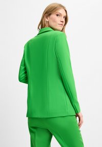 Grüner Blazer mit taillierter Passform, glatter Textur und breitem Revers. Verfügt über lange Ärmel und ein elegantes Design, kombiniert mit passenden Hosen.