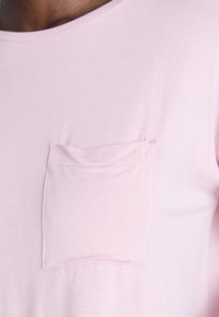 Närbild av en ljusrosa t-shirt med en liten sydd bröstficka på vänster sida.