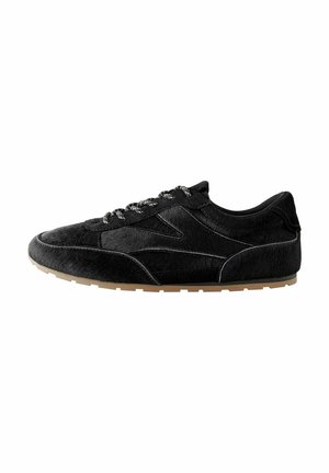 Scarpa sportiva nera realizzata in materiale morbido e testurizzato con un design elegante. Presenta lacci decorati e una suola in gomma naturale.