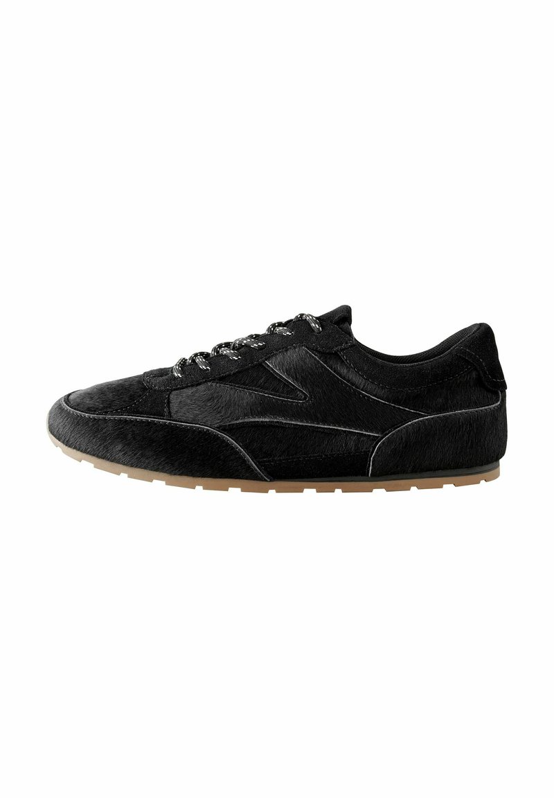 Scarpa sportiva nera realizzata in materiale morbido e testurizzato con un design elegante. Presenta lacci decorati e una suola in gomma naturale.