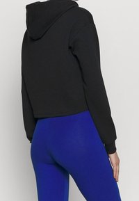 Sweat à capuche court noir avec une capuche, en tissu doux, associé à des leggings bleus à fort contraste, affichant une texture lisse.