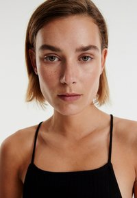 Zwarte geribbelde tanktop met dunne bandjes, voorzien van een vierkante halslijn. De stof lijkt zacht en lichtjes textuur te hebben. Neutraal achtergrond.