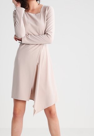 Vestido beige de manga larga con escote cuadrado, dobladillo asimétrico y textura suave. Diseño drapeado que añade dimensión.