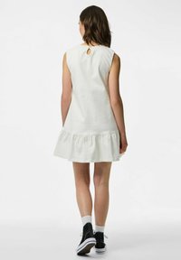 Balta bez piedurknēm tērps ar viļņotām malām un atvērtiem detalizējumiem aizmugurē, izgatavots no mīksta auduma, apvienots ar melniem augstiem sporta apaviem un baltām zeķēm.