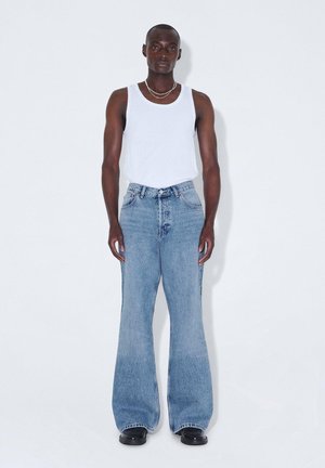 Jeans a zampa d'elefante in denim azzurro chiaro con vita alta, abbinati a una canotta bianca senza maniche. Calzature nere e collane sovrapposte semplici.