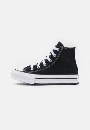 Črn visok sneaker iz platna z belo gumijasto podplatom, ki ima bele vezalke in kontrastne šive, zaobljen nos, ter črne črtne akcentne podrobnosti.