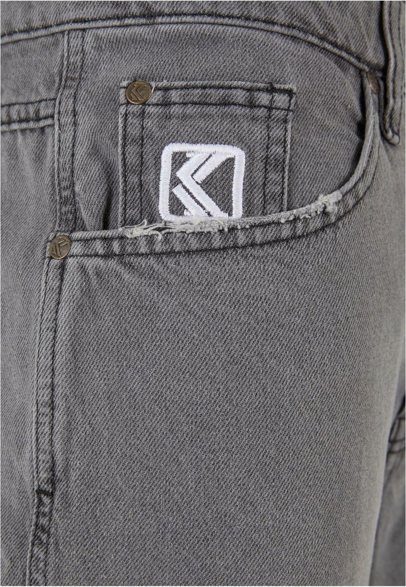 Shorts en denim gris avec un bord de poche effiloché et un patch logo brodé blanc. Des accents en métal agrémentent le design.