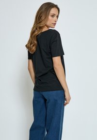 Camiseta negra de manga corta con cuello redondo, de corte relajado, combinada con pantalones de mezclilla azul de pierna ancha. Textura suave, diseño minimalista.