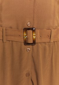 Brun midje-klänning med knapplås framtill, med en stor rektangulär sköldpaddsbälte och slätt, texturerat tyg.