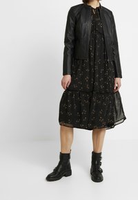 Czarna skórzana kurtka z wysokim kołnierzem na czarnej sukience w kwiatowy wzór. Do kompletu masywne czarne botki za kostkę z paskami i klamrami.