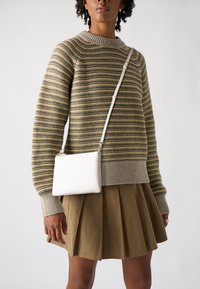 Stripet strikkegenser i beige og oliven, med bred hals; sammen med en plisserte khaki skjørt. Hvit strukturert crossover-veske henger på siden.