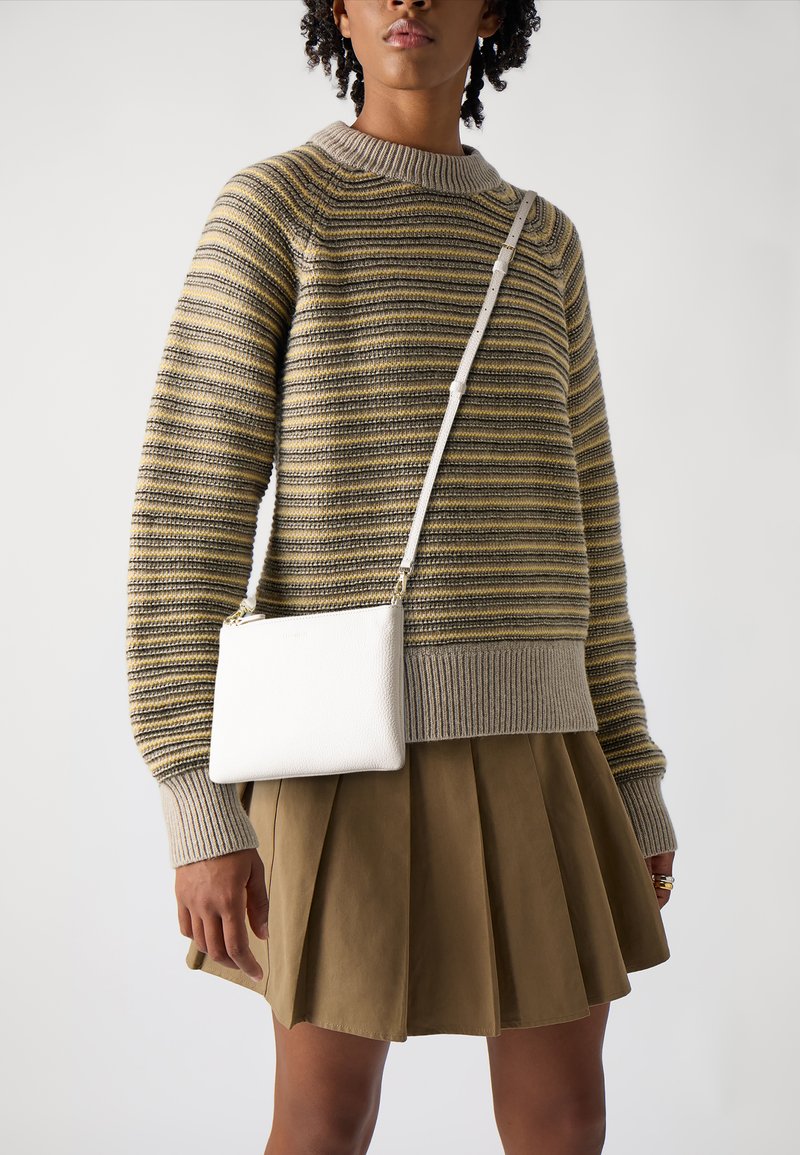 Stripet strikkegenser i beige og oliven, med bred hals; sammen med en plisserte khaki skjørt. Hvit strukturert crossover-veske henger på siden.