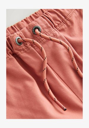 Shorts v bledem koralnem odtenku, izdelani iz mehkega blaga z elastičnim pasom, ki vsebuje vrvico z črnimi detajli in kovinskimi okovji.