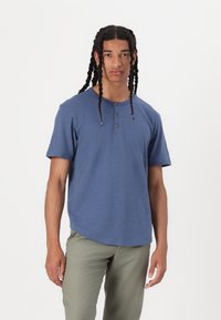 Korte ermet blåt henley skjorte med tre træknapper, rundudskæring og en afslappet pasform. Sammen med lysegrønne bukser, minimalistisk design.