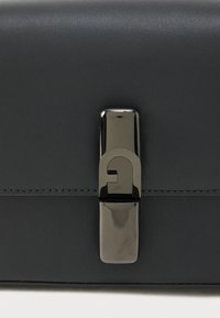 Melnas ādas soma ar spīdīgu melnu aizdares sprādzi un šuvju detaļām. Gluda tekstūra ar elegantu taisnstūra formu.