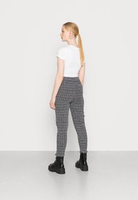 Calças ajustadas em padrão xadrez preto e branco com uma cintura alta e tecido texturizado, combinadas com uma t-shirt branca cropped e botas pretas com atacadores.