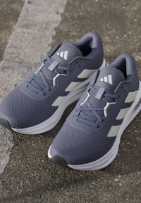 Gray athletic shoes with a textured upper, featuring white accents and laces, a cushioned sole, and a modern design.