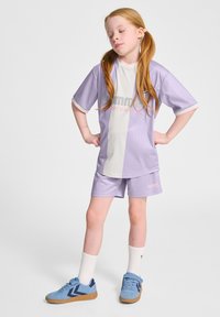 Lila sportströja med vit mittsektion och logotyp, i kombination med matchande shorts. Accentdetaljer inkluderar ribbat mönster och kontrasterande kant.