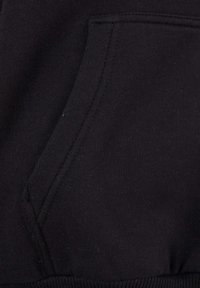 Black sweatshirt material with a front pocket. Soft texture, ribbed hem at the bottom, and visible stitching along the pocket edges.
