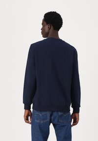 Marineblå bomullsgenser med lange ermer, ribbede mansjetter og hals, og en avslappet passform, kombinert med blå denimjeans.