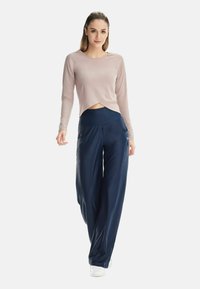 Hellrosa langärmeliges Oberteil mit kurzem Schnitt, kombiniert mit locker sitzenden dunkelblauen Hosen, beide aus glattem, leichtem Stoff gefertigt.