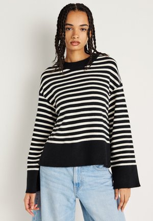 Pull rayé noir et crème, avec un encolure ras du cou, une coupe décontractée et des manches longues. Fabriqué en tissu tricoté doux.