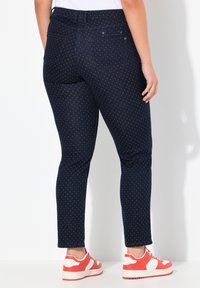 Tmavě modré džíny s potiskem puntíků, úzký střih, elastický pas a dvě zadní kapsy, doplněné červenými a bílými teniskami.