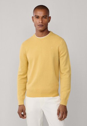 Gelber Rundhalsausschnitt-Pullover aus weichem Stoff mit gerippten Bündchen und Saum. Verfügt über ein kleines Logodetail auf der Brust. Trägt man mit weißen Hosen.