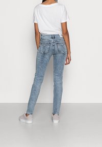 Světle modré, vysoké skinny džíny s vybledlým omakem. Obsahují dvě zadní kapsy s zakřiveným stehem a přiléhavý design.