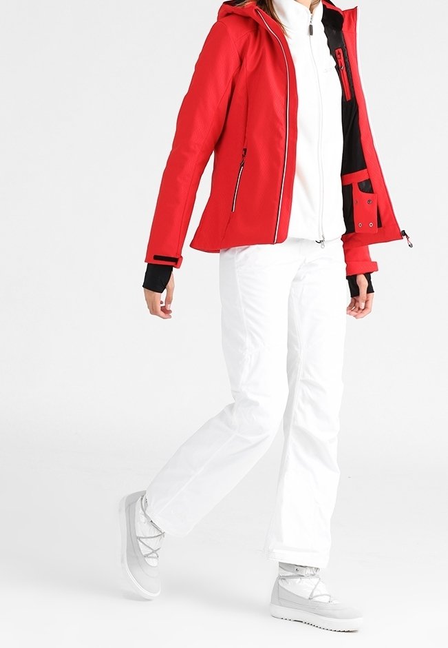 Rød isoleret jakke med hætte, lynlås foran og sorte detaljer. Bæres med hvide bukser og gråt fodtøj. Glat, tekstureret overflade.