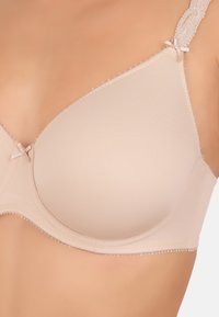 Lys beige bh med glat stof, formede skåle, delikate blonde-stropper og dekorative buer ved stroppernes samlinger. Akcentueret med subtile perledetaljer.