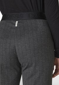 Graue, strukturierte Hose mit vertikalen Streifen, einem dicken schwarzen elastischen Bund mit eingeprägtem Logo und einem kleinen Etikett mit Markenname.