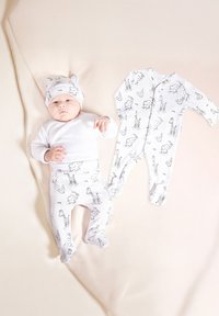 Biały niemowlęcy strój składający się z koszuli z długim rękawem, spodni z wzorem zwierząt oraz dopasowanej czapki z uszami, ułożony na miękkim beżowym tle.