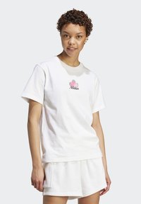 Vit bomullströja med rund halsringning och korta ärmar, prydd med en design av en ananas i rosa och grönt, samt texten "Adidas".