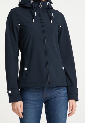 Femme portant une veste zippée bleu marine avec des détails de boutons blancs, une capuche ajustable avec cordons de serrage, et un jean bleu.