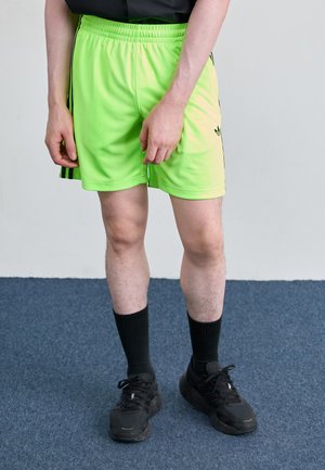 Neon green athletic shorts with an elastic waistband, black stripes, and logo. Paired with black knee-high socks and black sneakers.