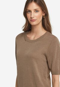 Brun strikket T-shirt med kortærmer, rund halsudskæring, glat tekstur og subtile ribbede detaljer ved kraven og ærmerne.