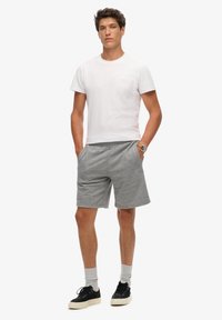 Camiseta blanca de algodón y pantalones cortos de jersey grises. Los pantalones cortos cuentan con una cinturilla elástica y bolsillos, combinados con zapatillas negras y calcetines grises.