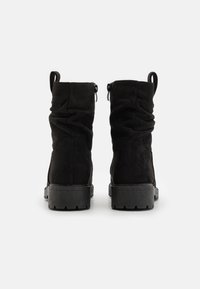 Černé semišové kotníkové boty se skládacím designem, zipovým uzávěrem a texturovanou gumovou podrážkou. Obsahují dvě poutka na zadní straně.