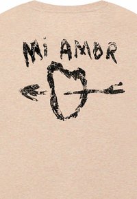 Beige katoenen t-shirt met een zwarte grafische print van een hart met een pijl en de tekst "Mi Amor" erboven. Korte mouwen en ronde hals.