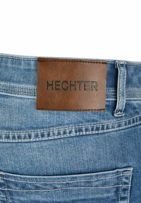 Lichtblauwe spijkerbroek van denim met een bruine leren taille-label met de opdruk "HECHTER." Voorzien van contrasterende stiksels en achterzakken.