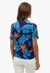 Korte mouwen overhemd in marineblauwe stof met een levendig tropisch bladpatroon in blauw, groen en rood. Ontwerp met kraag en een rechte zoom.