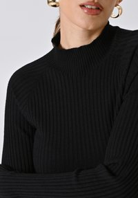 Maglione a coste nero con colletto alto e maniche lunghe, caratterizzato da un tessuto testurizzato e un design aderente.