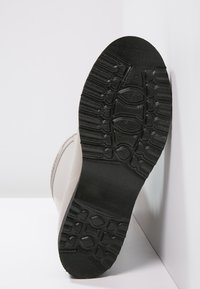Semelle de botte en caoutchouc noir avec un motif de semelle texturé ; partie supérieure gris clair visible, matériau lisse, conçu pour l'adhérence et la durabilité.
