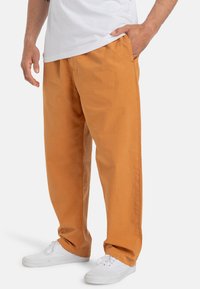 Orange cotton pants with a relaxed fit, featuring side pockets and a smooth texture. Worn with white sneakers.