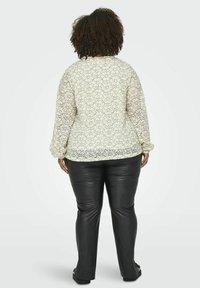 Blusa di pizzo in bianco sporco con un motivo floreale, maniche arricciate, abbinata a pantaloni di pelle nera. Tessuto testurizzato e semitrasparente.