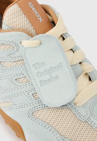 Ανοιχτό μπλε και μπεζ αθλητικό παπούτσι με παχιές κρεμ κορδόνια, καφέ πάτο με την ένδειξη Geox, και ταμπέλα από σουέντ με την επιγραφή "The Original Snake" προσαρτημένη στα κορδόνια.