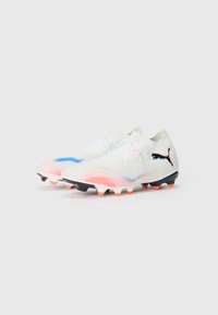 Weiße Fußballschuhe mit einer strukturierten Oberseite, die blaue und pinke Farbverläufe, schwarze Akzente und sechs genoppte schwarze und orange Sohle aufweisen.